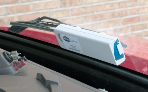 The inside of a red truck, a white Bestpass transponder is attached to the inner windshield 